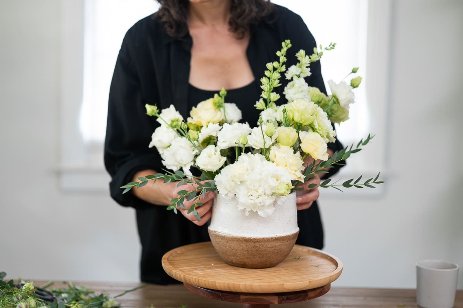 female florist arranging white flowers in a white and clay colored round vase